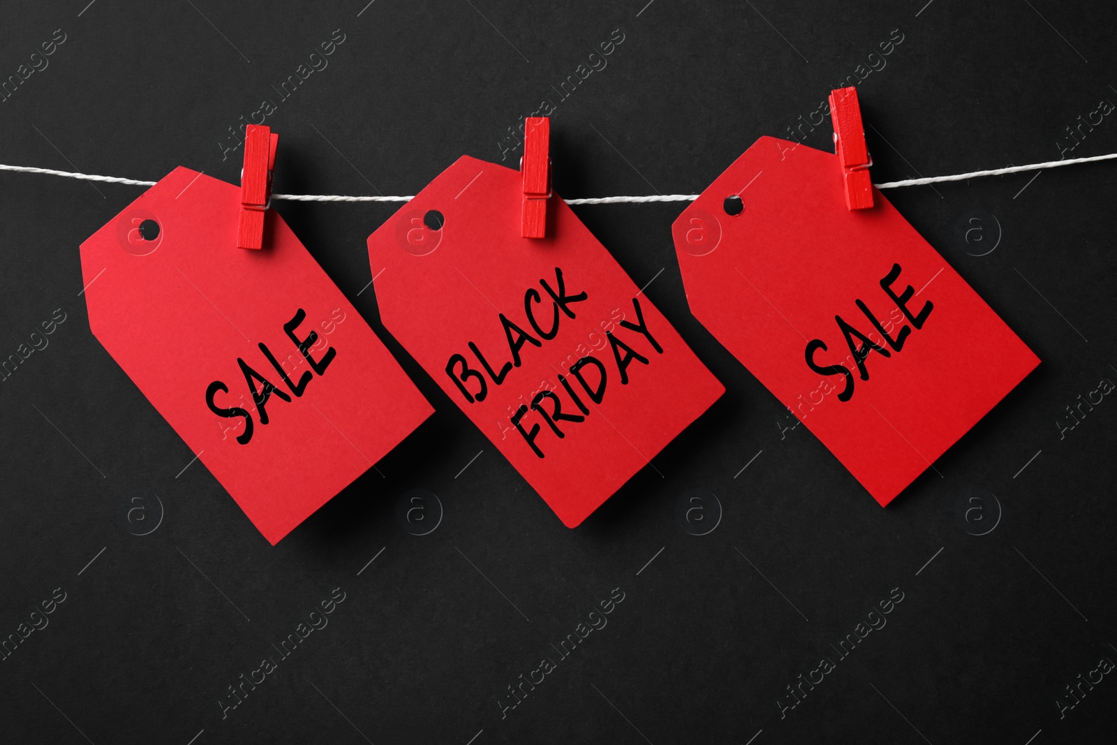 Photo of Red tags with text Black Friday and Sale on rope against color background