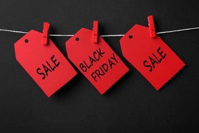 Photo of Red tags with text Black Friday and Sale on rope against color background
