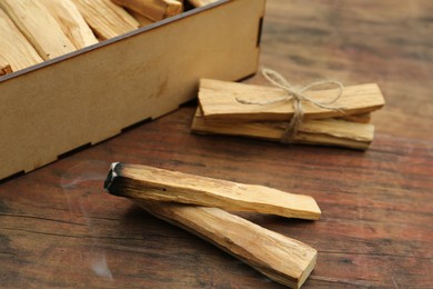 Many Palo Santo sticks and one smoldering on wooden table