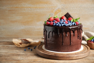 Photo of Freshly made delicious chocolate cake decorated with berries on wooden table