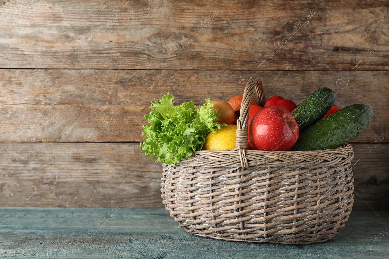 Photo of Wicker basket with ripe fruits and vegetables on color wooden table. Space for text