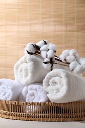 Photo of Rolled soft towels and cotton branch on white table indoors