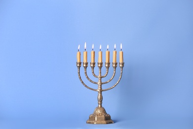 Photo of Golden menorah with burning candles on light blue background, space for text