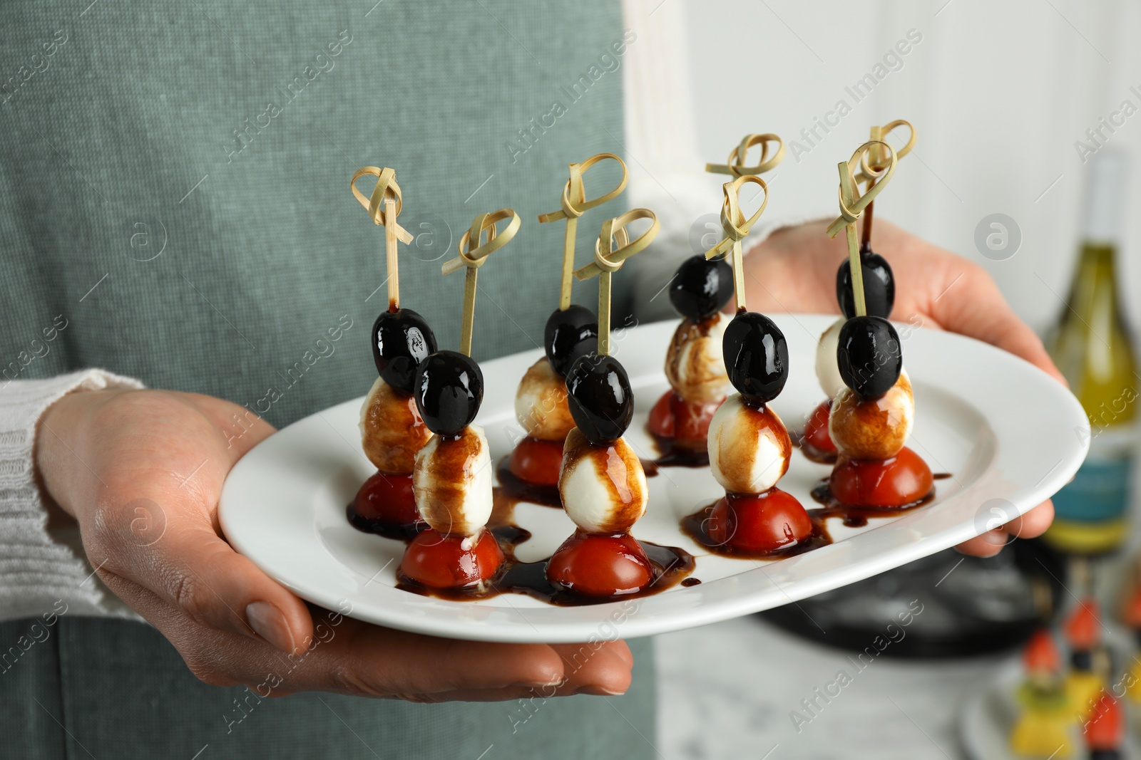 Photo of Woman holding plate of tasty canapes with black olives, mozzarella and cherry tomatoes indoors, closeup