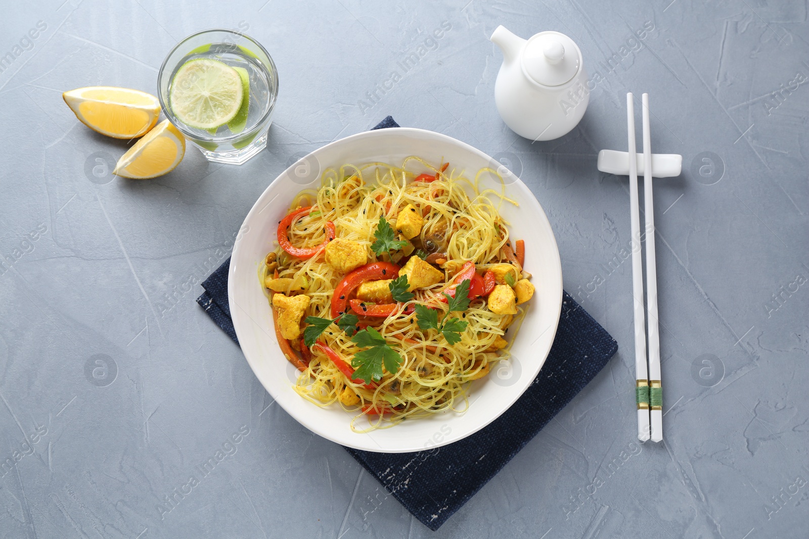 Photo of Stir-fry. Delicious cooked noodles with chicken and vegetables in bowl served on gray textured table, flat lay