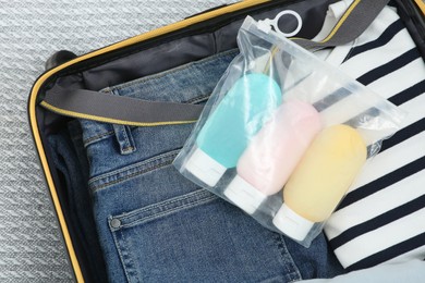 Plastic bag of cosmetic travel kit and clothes in suitcase, top view. Bath accessories