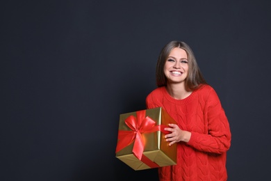 Photo of Young woman with Christmas gift on dark background. Space for text