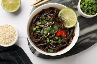 Photo of Tasty buckwheat noodles (soba) served on white table, flat lay