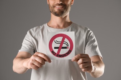 Photo of Man holding card with no smoking sign on gray background, closeup