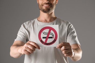 Man holding card with no smoking sign on gray background, closeup