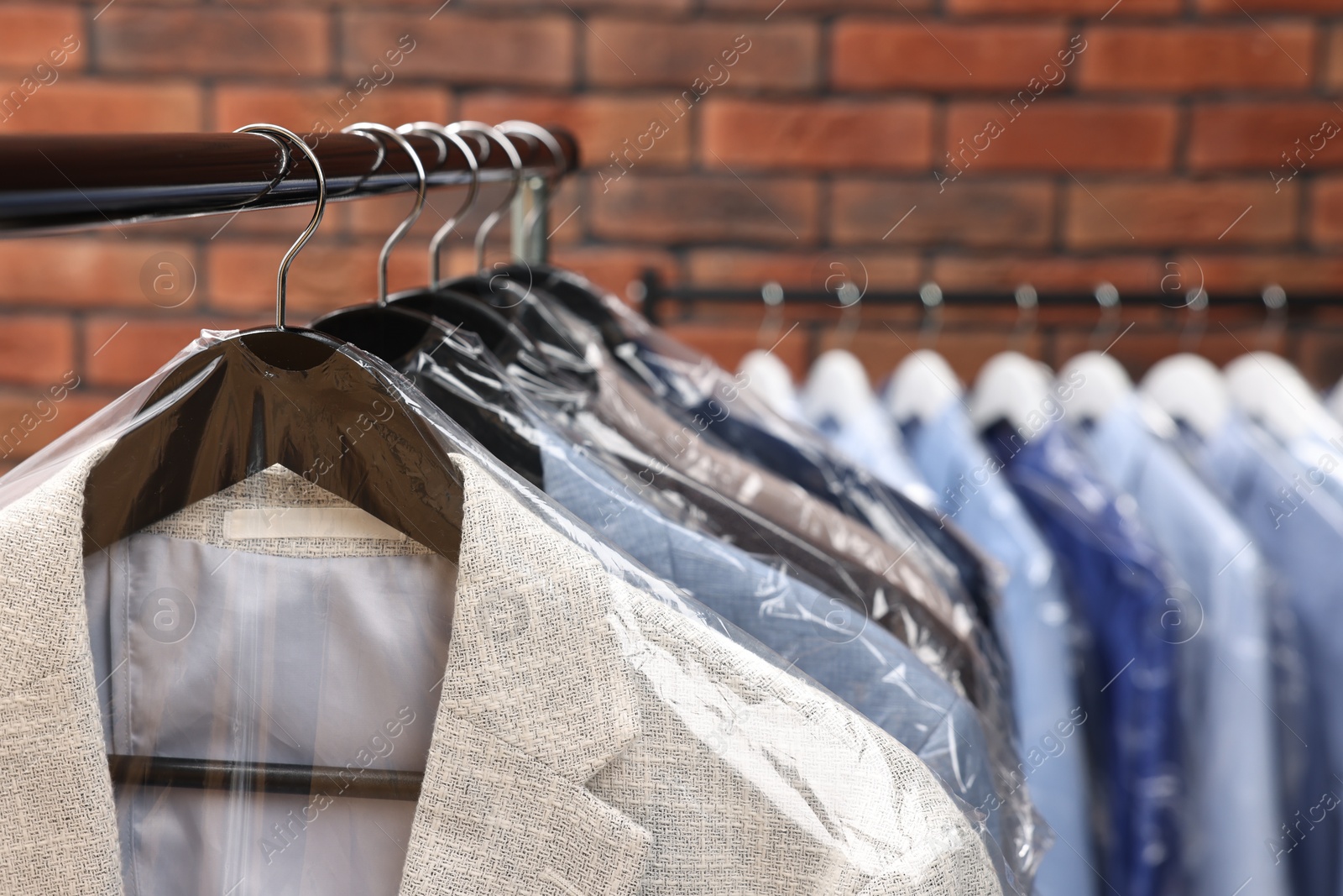 Photo of Dry-cleaning service. Many different clothes hanging on rack against brick wall, closeup