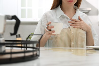 Photo of Woman with spilled coffee over her shirt at table in kitchen, closeup