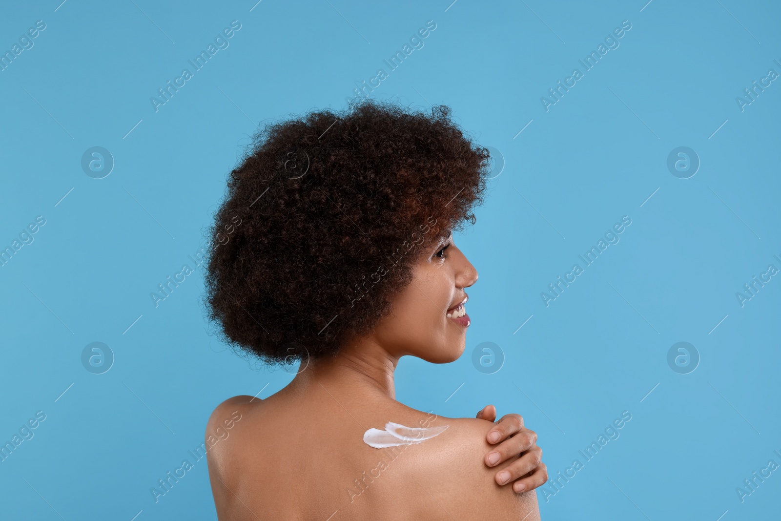 Photo of Beautiful young woman applying body cream onto back on light blue background