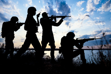 Silhouettes of soldiers with assault rifles patrolling outdoors. Military service
