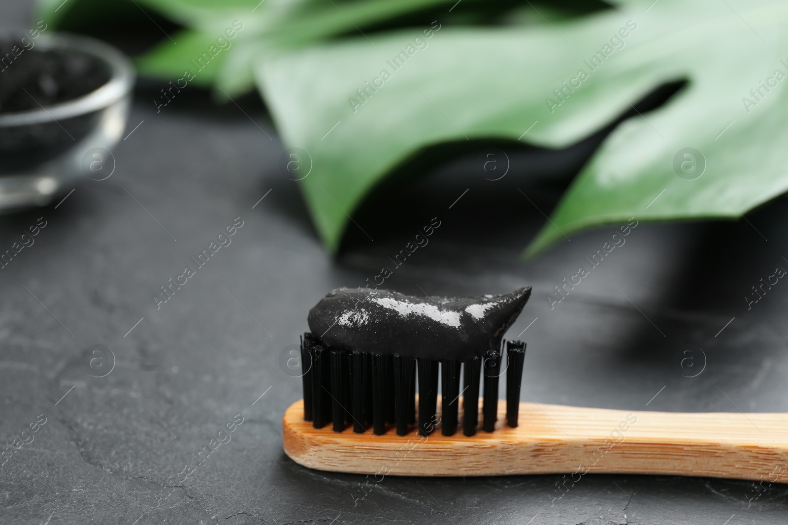 Photo of Bamboo toothbrush with charcoal paste on black stone table, closeup. Space for text