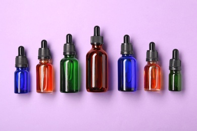 Bottles of essential oils on color background, flat lay. Cosmetic products