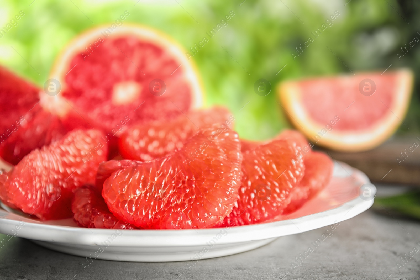 Photo of Plate with ripe grapefruit on table against blurred background