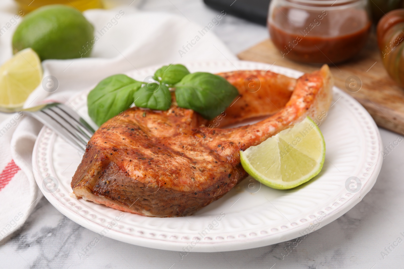 Photo of Freshly cooked fish, lime and basil on white marble table, closeup