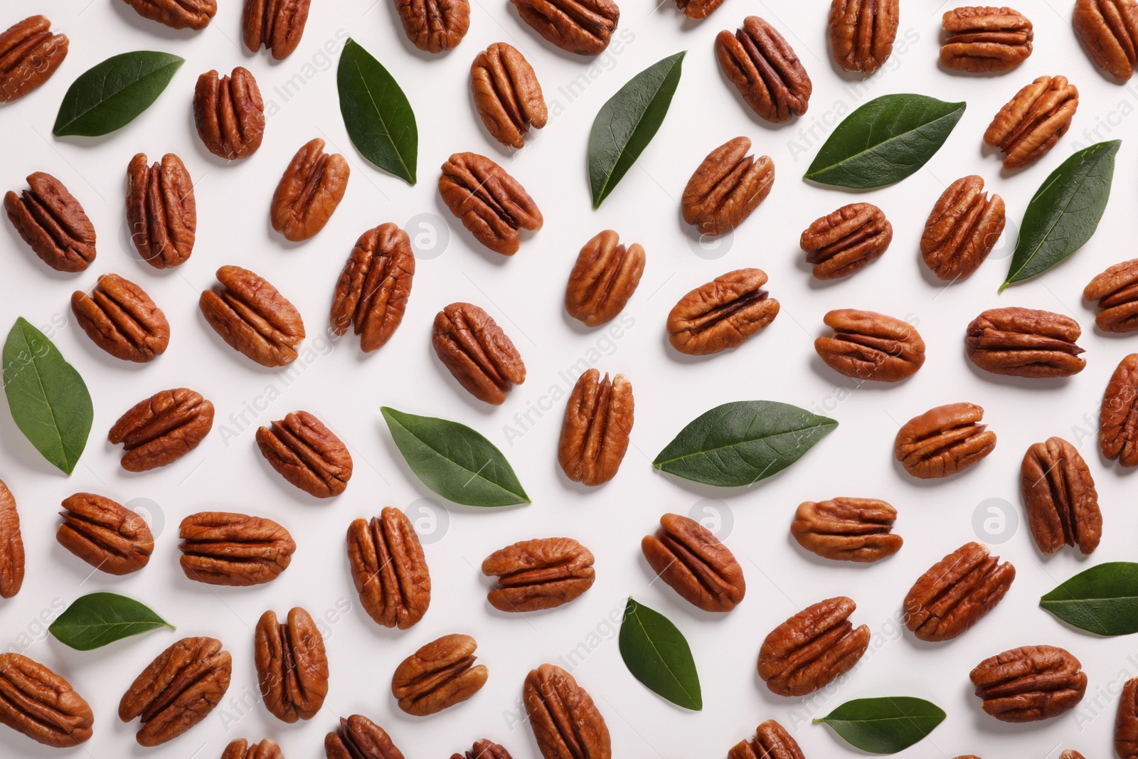 Photo of Delicious pecan nuts and green leaves on white background, flat lay