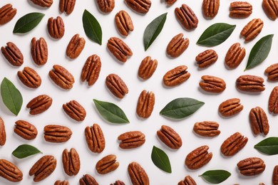 Delicious pecan nuts and green leaves on white background, flat lay
