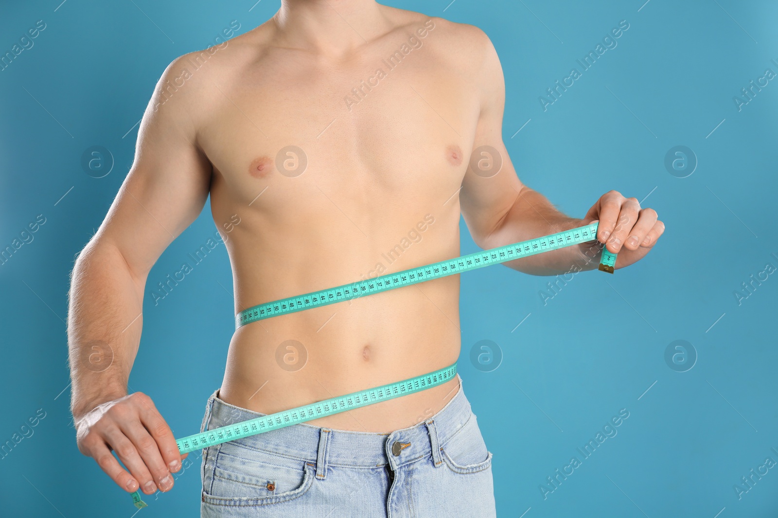 Photo of Man with slim body measuring his waist on color background, closeup