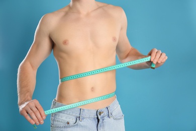 Man with slim body measuring his waist on color background, closeup