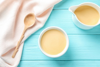 Photo of Flat lay composition with bowl and jug of condensed milk on wooden background