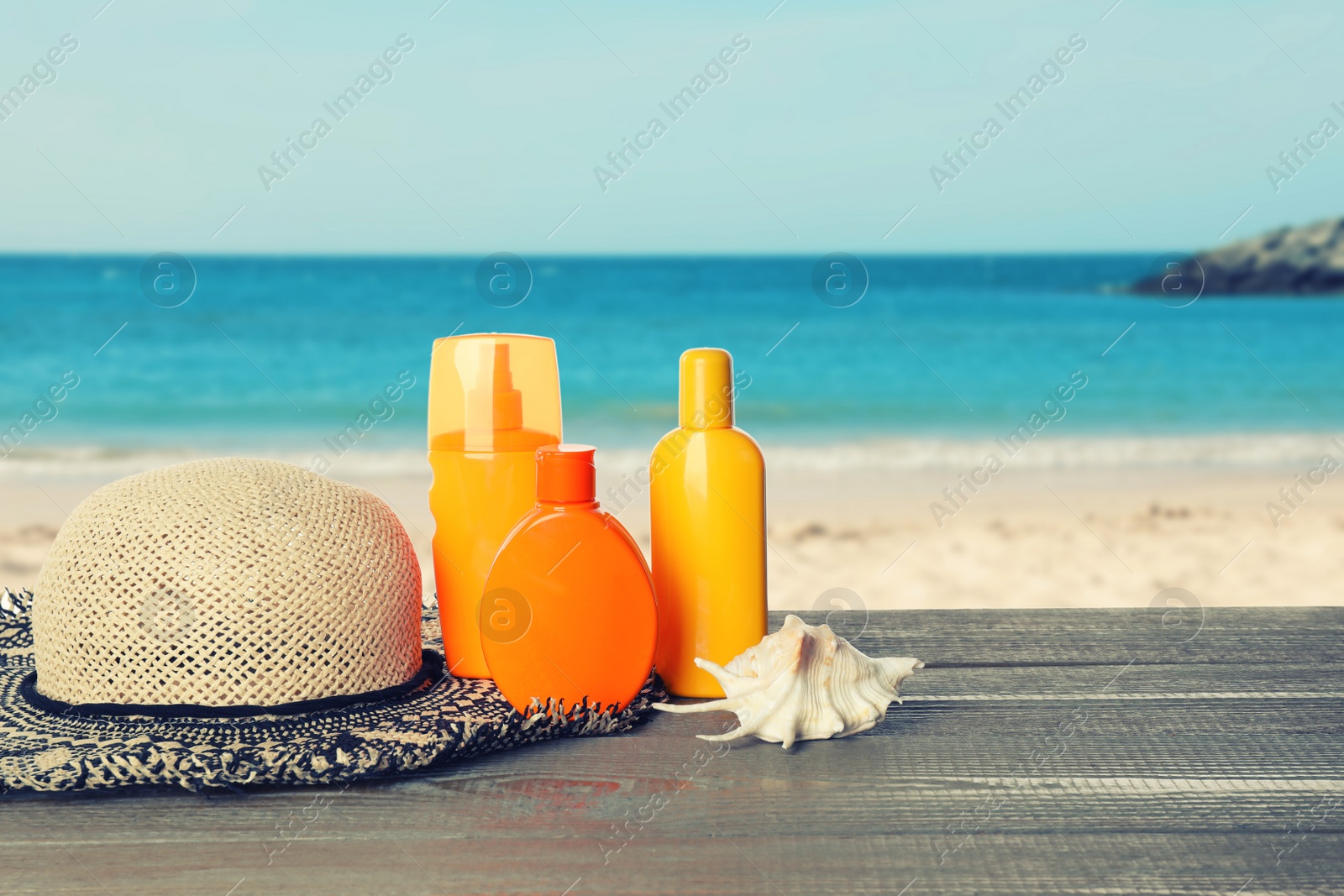 Image of Set of sun protection products and stylish hat on wooden table near sea. Space for text