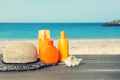 Image of Set of sun protection products and stylish hat on wooden table near sea. Space for text