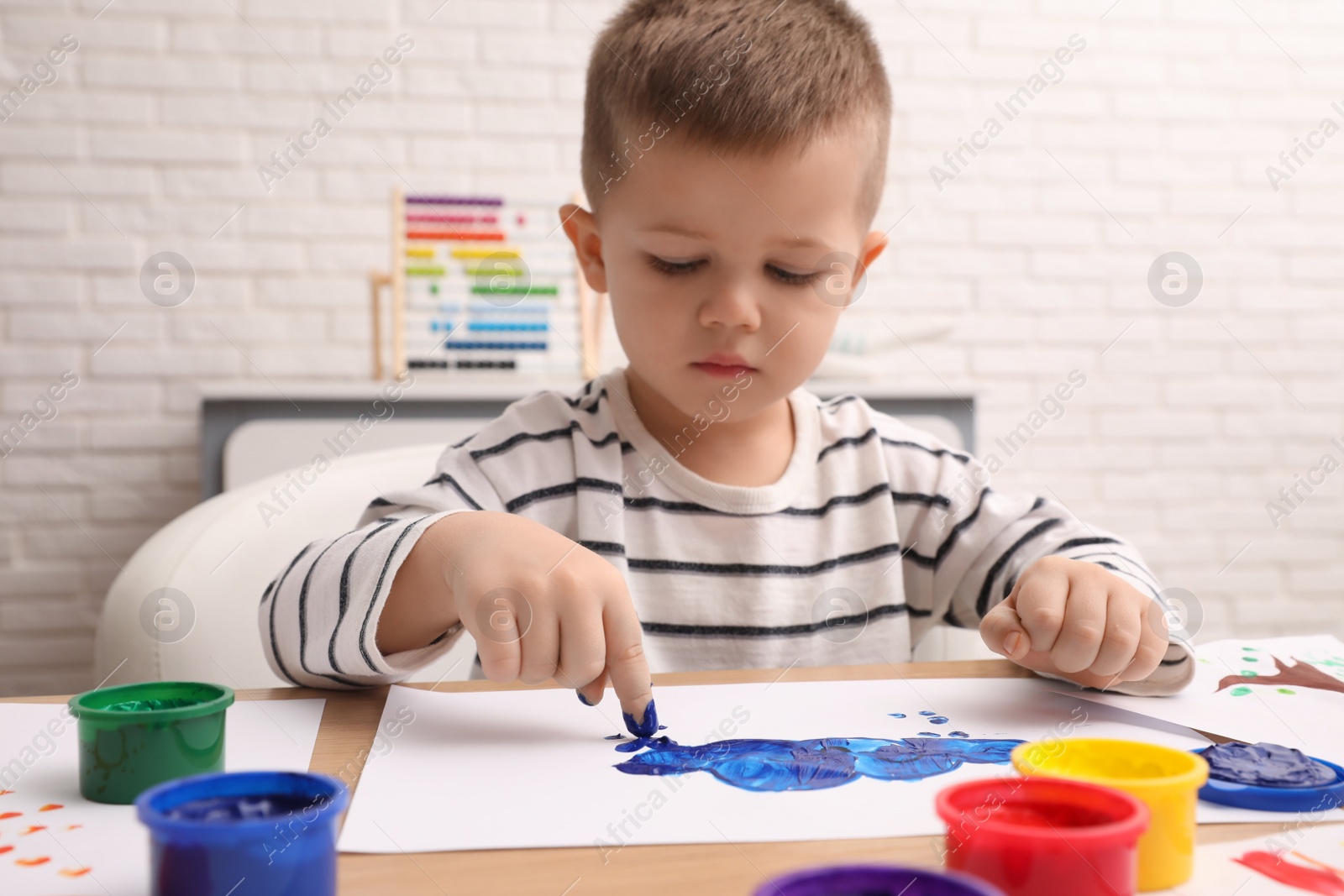 Photo of Little boy painting with finger at wooden table in room