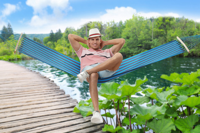 Image of Man resting in hammock near river on sunny day 
