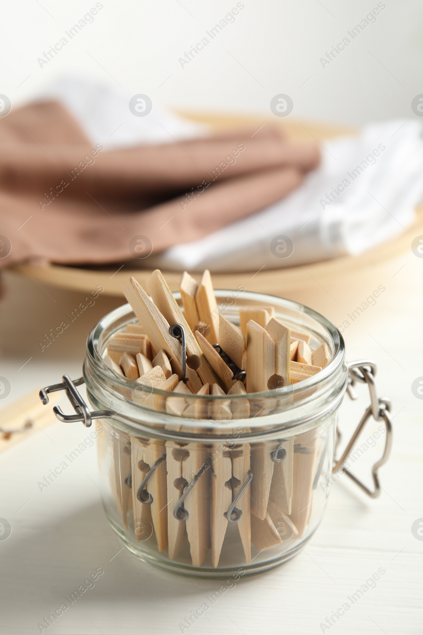 Photo of Many wooden clothespins and glass jar on white table