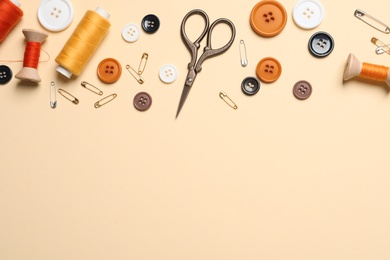 Photo of Flat lay composition with scissors and other sewing accessories on light yellow background, space for text