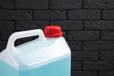 Photo of Plastic canister with blue liquid against dark brick wall, closeup. Space for text