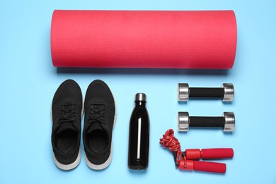 Photo of Exercise mat, dumbbells, bottle of water, skipping rope and shoes on light blue background, flat lay