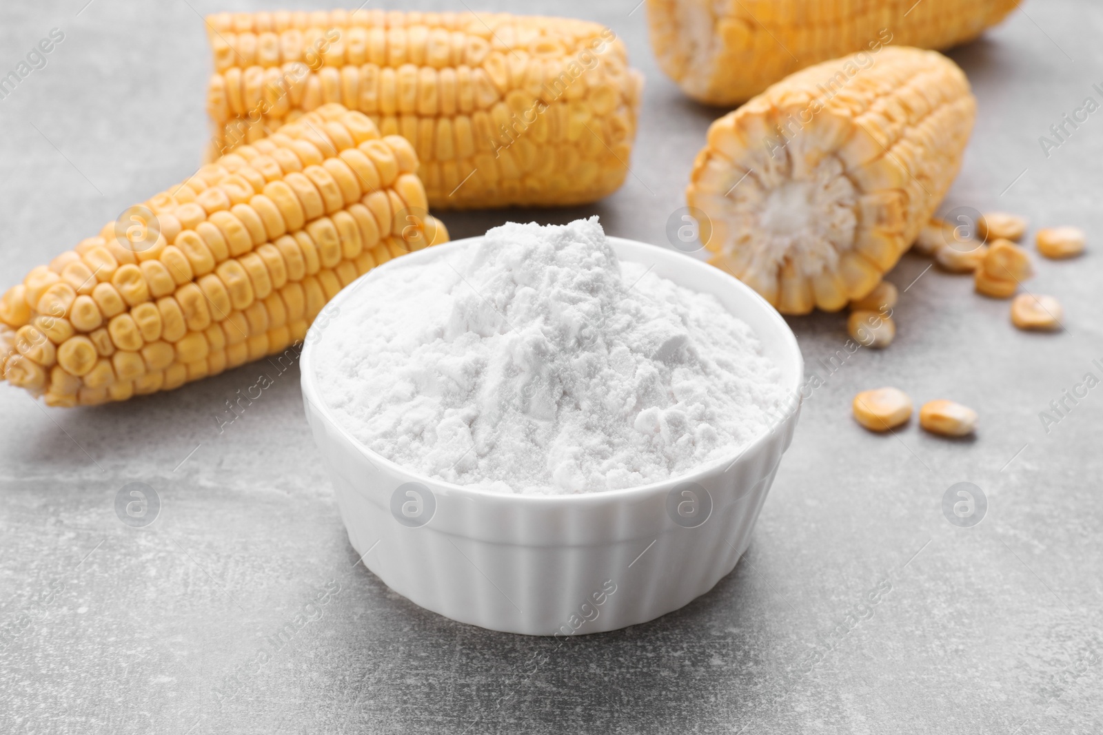 Photo of Bowl with corn starch and ripe cobs on light grey table, closeup