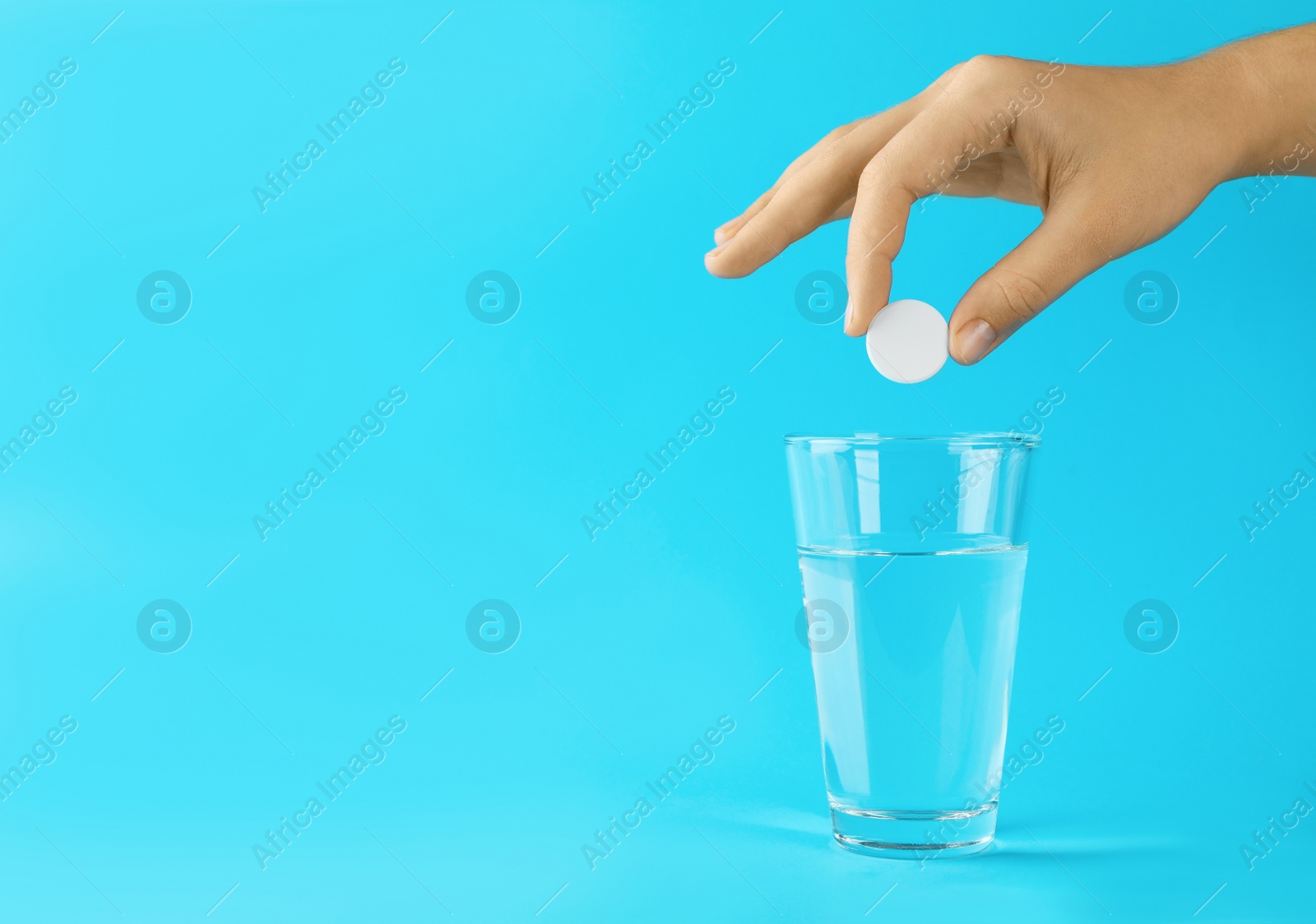 Photo of Woman putting tablet into glass of water on light blue background, space for text