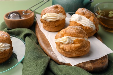 Photo of Delicious profiteroles filled with cream and tea on green background