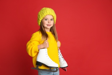 Photo of Cute little girl in yellow knitted sweater with skates on red background, space for text