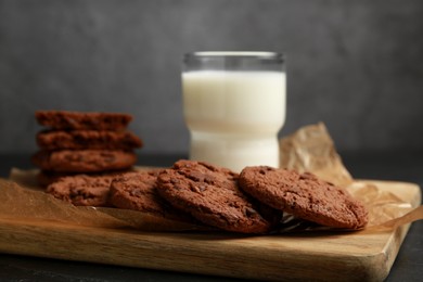 Photo of Board with tasty chocolate cookies and glass of milk on table, closeup