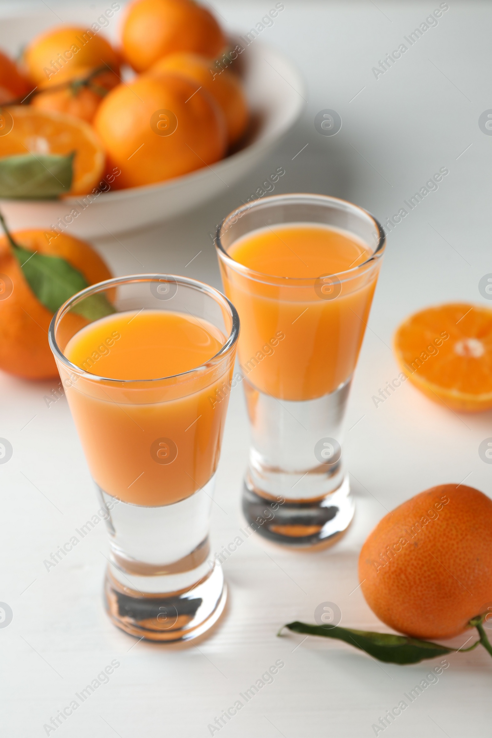 Photo of Tasty tangerine liqueur in shot glasses and fresh fruits on white table