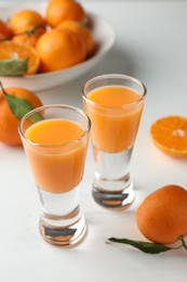 Photo of Tasty tangerine liqueur in shot glasses and fresh fruits on white table