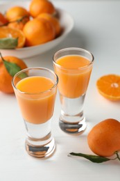 Tasty tangerine liqueur in shot glasses and fresh fruits on white table