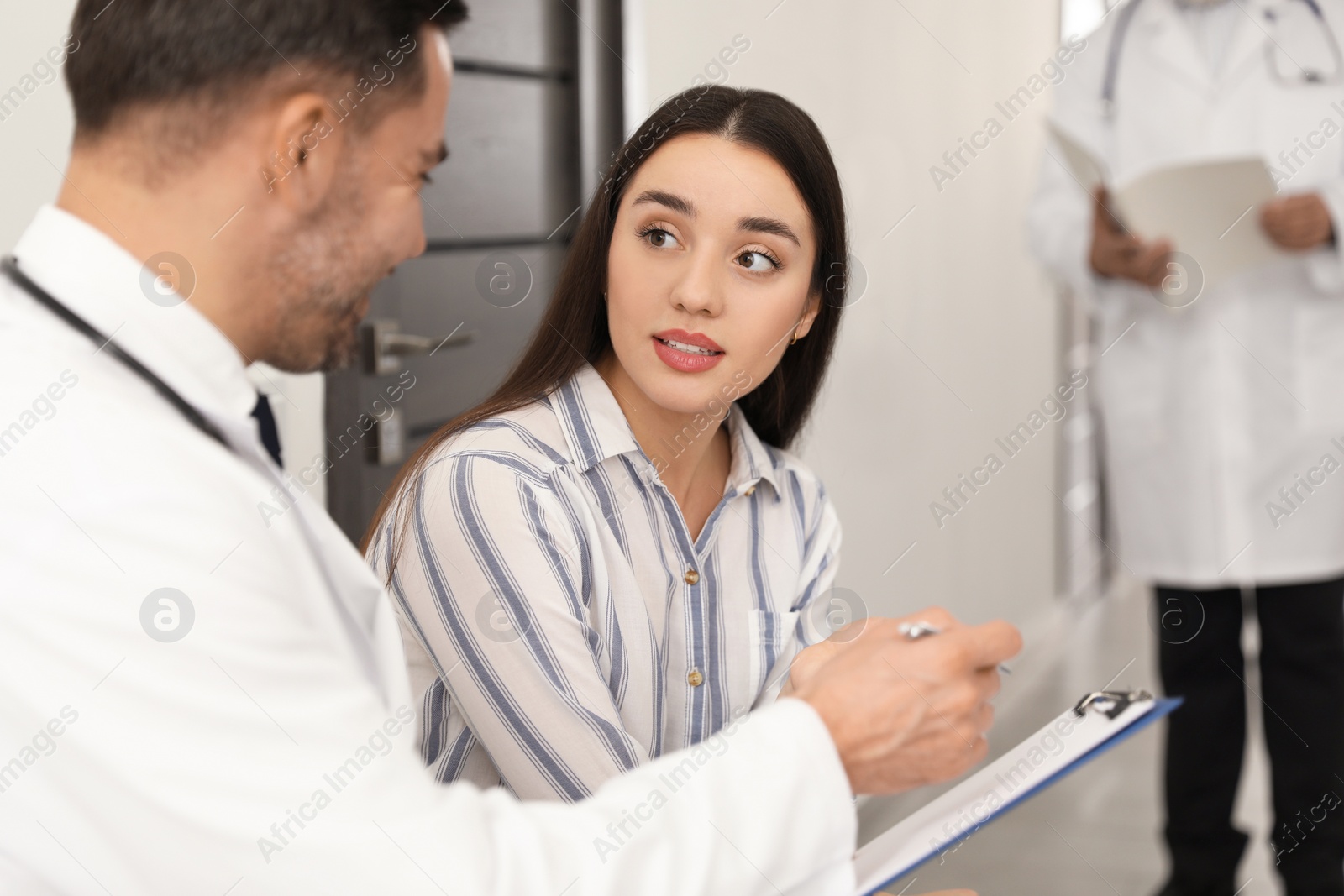 Photo of Doctor with clipboard consulting patient in clinic