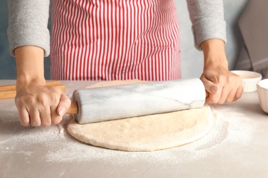 Woman rolling dough for cinnamon rolls on table, closeup