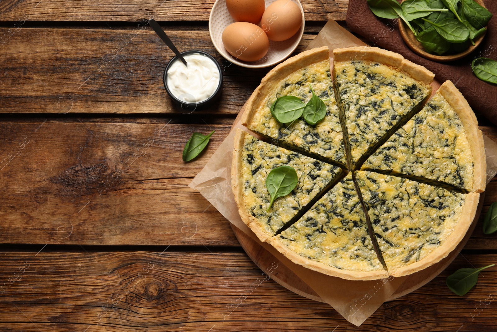 Photo of Cut delicious spinach pie with ingredients on wooden table, flat lay. Space for text