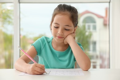Photo of Little girl solving sudoku puzzle at table indoors