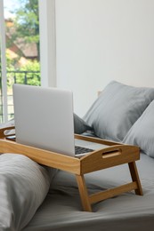 Photo of Wooden tray table with laptop on bed indoors