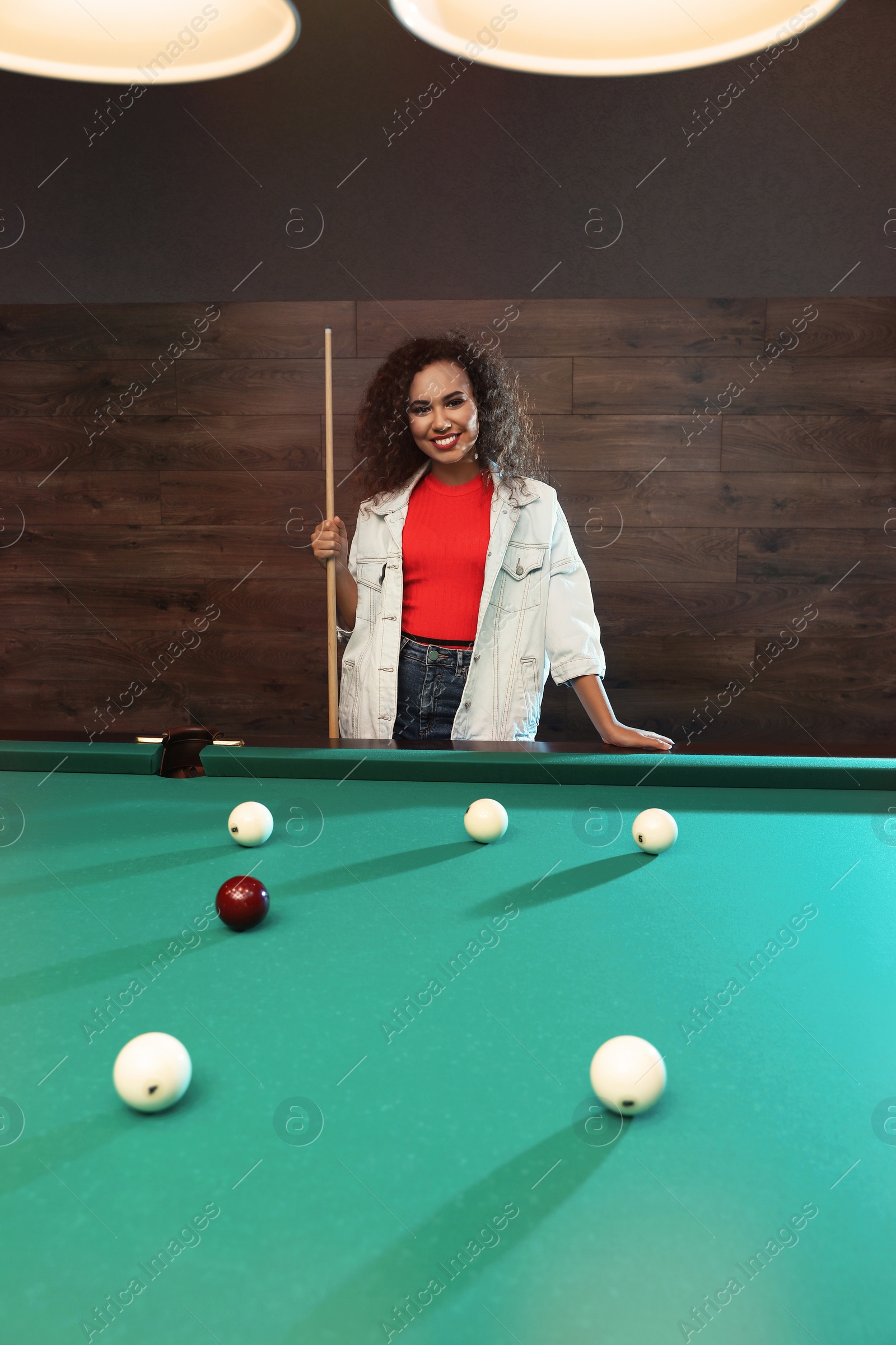 Photo of Young African-American woman with cue near billiard table indoors