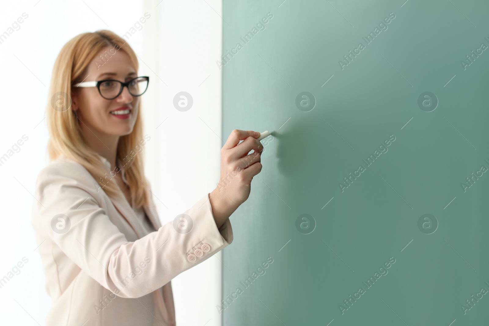Photo of English teacher writing on green chalkboard at lesson